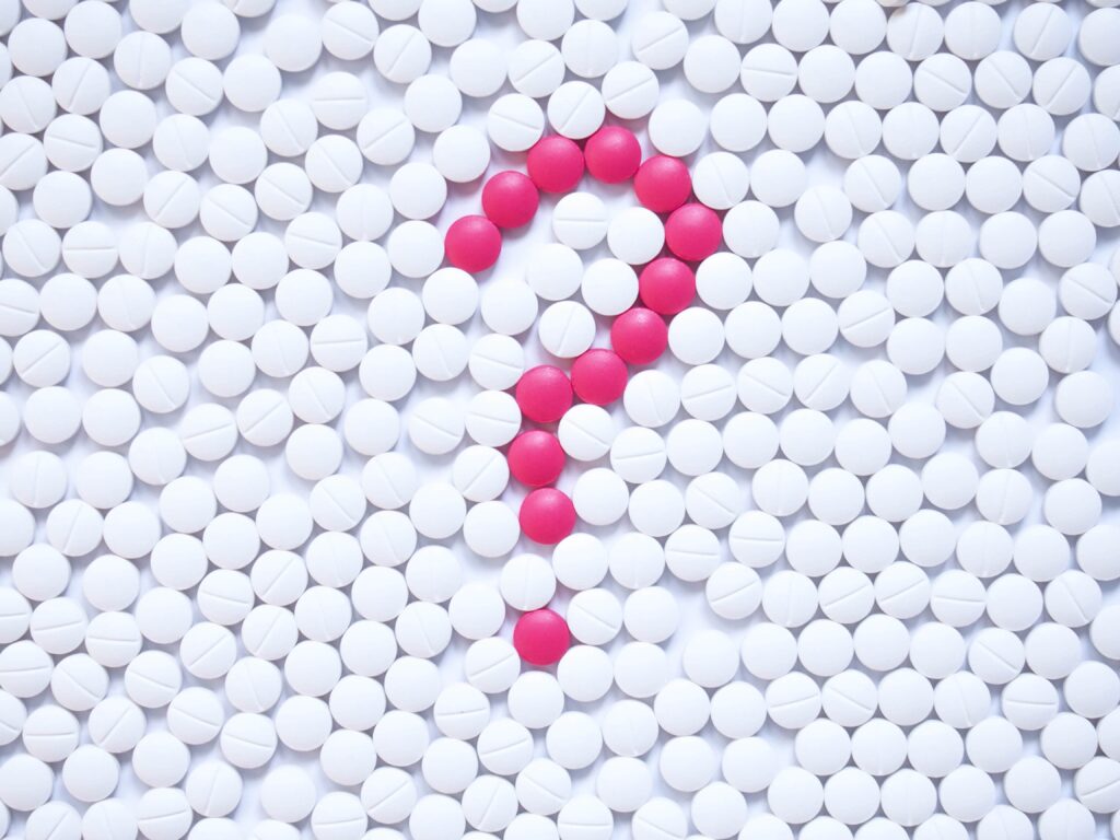 Question mark formed by pink pills among white ones background